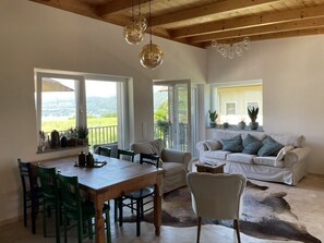 Amplia sala de estar con una mesa de comedor de madera, sillas verdes, un sofá blanco y un sillón de cuero.