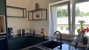 Une cuisine moderne avec un plan de travail noir, des appareils en acier inoxydable et une fenêtre donnant sur une maison.