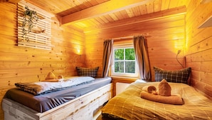 Une chambre dans un chalet en bois, avec deux lits, une fenêtre avec des rideaux et un luminaire fixé au mur.