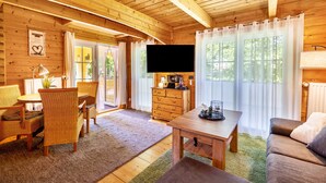 L’intérieur d’un chalet en bois comprend un coin repas, un canapé, un téléviseur et des fenêtres.