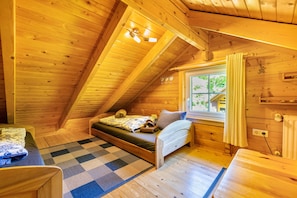 Un dormitorio acogedor en el ático, con techo inclinado, cama, una mesita y una ventana con cortinas.