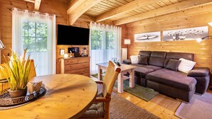 L’intérieur d’un chalet en bois comprend une table à manger, un canapé, un téléviseur et des œuvres d’art accrochées aux murs.