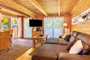 Interior de una cabaña de madera con sofá, televisor y comedor.
