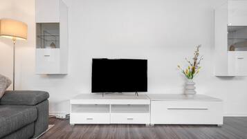 Ein modernes Wohnzimmer mit Flachbildfernseher, weißem Unterhaltungsschrank, grauem Sofa und einer Stehlampe.