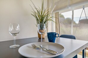 A dining table with a clear glass wine glass, a white plate with a fork and knife, a blue mug, and a potted plant with long green leaves. - Holiday Home 'Safarizelt' with Private Terrace, Wi-Fi and Air Conditioning (Großenbrode)