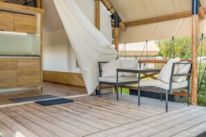Une terrasse en bois avec une table et des chaises, une structure en forme de tente et un meuble en bois.