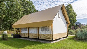 A single-story, A-frame tent with a beige canopy, set on a grassy area with trees in the background. - Holiday Home 'Safarizelt' with Private Terrace, Wi-Fi and Air Conditioning (Großenbrode)