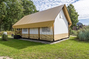 Une tente en forme de « A », d’un seul niveau, avec une toile de couleur beige, installée sur une pelouse, avec des arbres en arrière-plan.