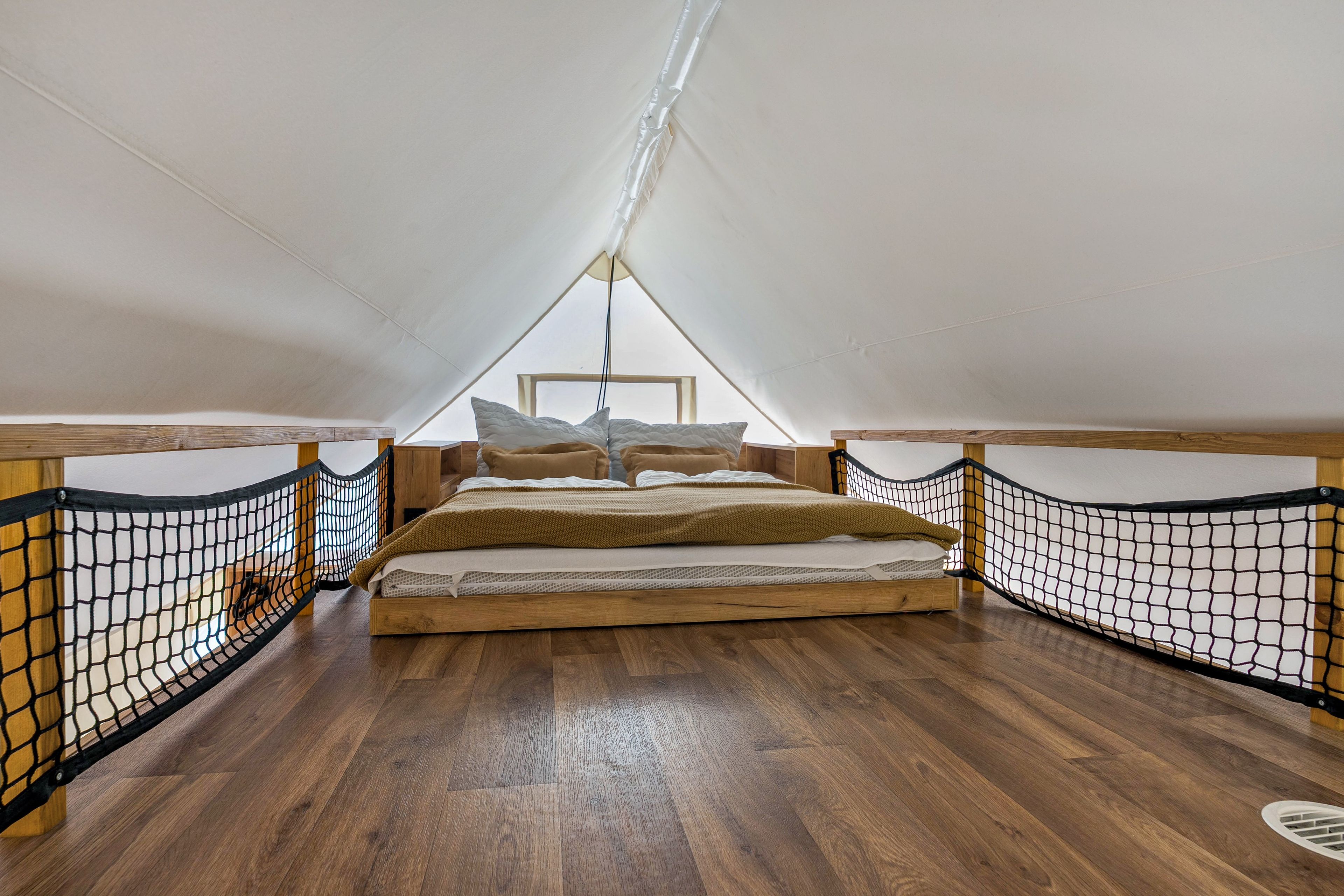 Un espacio pequeño y cerrado con cama, suelo de madera y barandillas de mosquitera.
