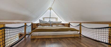 Un espacio pequeño y cerrado con cama, suelo de madera y barandillas de mosquitera.