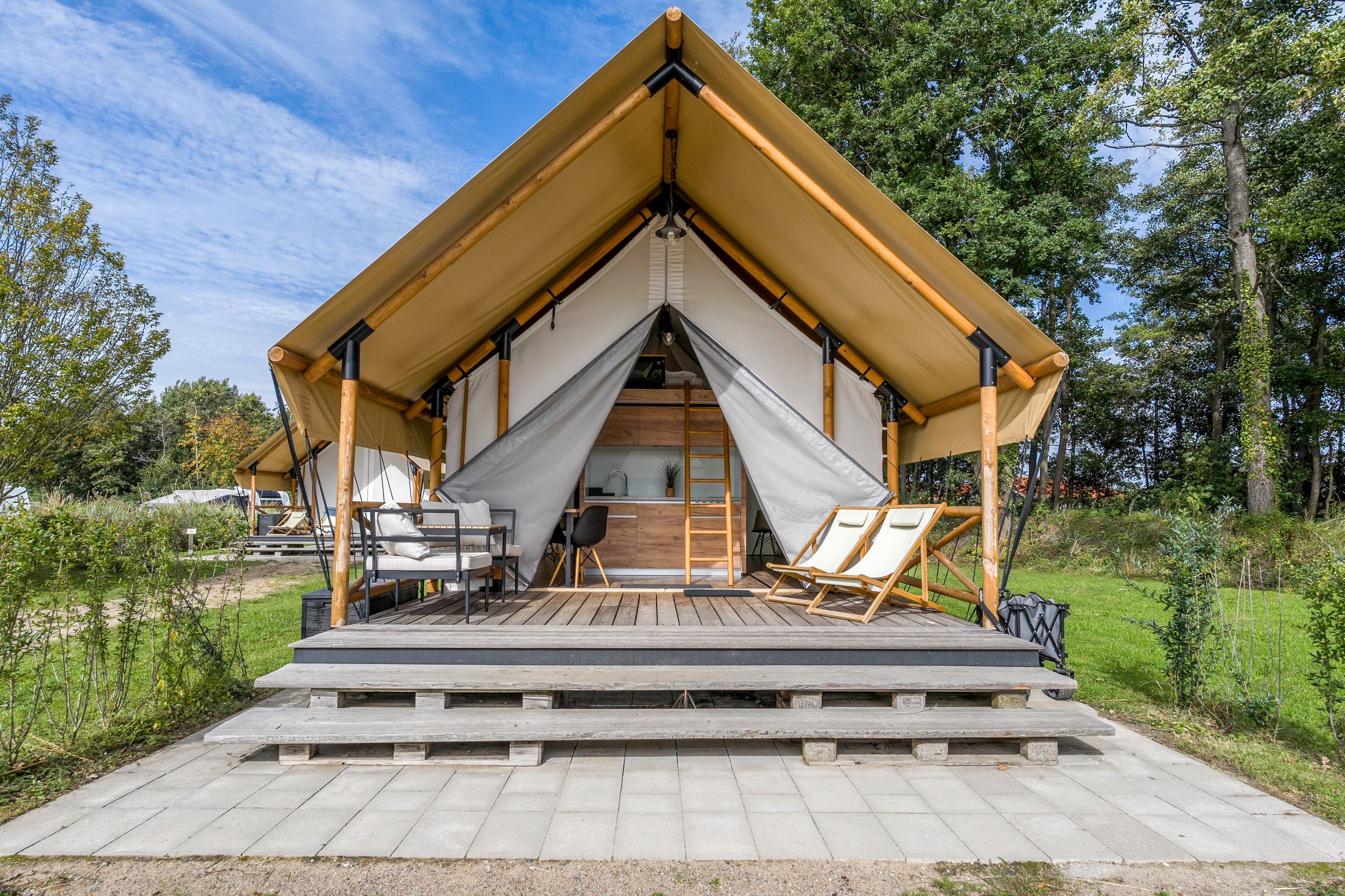 Eine moderne Unterbringung im Zeltstil mit Holzterrasse, Essbereich und Blick auf die umliegende Natur.