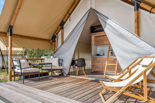 A tent with a wooden deck, outdoor seating, and a kitchen area.