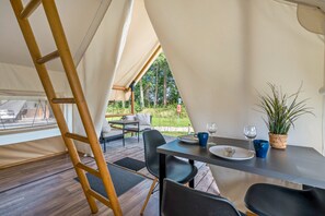 Un hébergement sous tente comprenant un espace repas, une échelle et une vue sur l’extérieur.