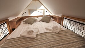 Ein gemütlicher, dreieckiger Zeltraum mit Bett, Kissen und ordentlich gefalteten Handtüchern.