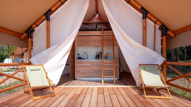 Eine Holzterrasse mit einer Küchenzeile, zwei Liegestühlen und einer Leiter zu einem Schlafbereich im oberen Geschoss.