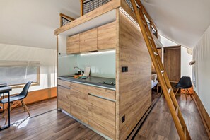 A compact kitchen with wooden cabinetry, a built-in stove, and a dining area with a chair and table.