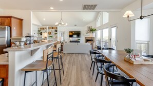 A modern kitchen with a central island, wooden bar stools, and a dining area with a long table. - Private Hill Country Pool Retreat w/ Skyline Views (Canyon Lake)