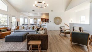 A spacious living room with a large sofa, ottoman, and chairs, a dining area, and a kitchen in the background. - Private Hill Country Pool Retreat w/ Skyline Views (Canyon Lake)