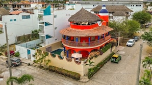 A multi-story building with a red and white color scheme, a thatched roof, and a balcony with railings. - Golden Zone 5 Blocks to Beach - Groundfloor w Pool (Bucerías)