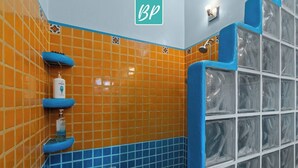 Ein Badezimmer mit orangefarbenen und blauen Fliesen, einem Handtrockner und einer Duschkabine aus Glas.