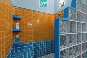 Ein Badezimmer mit orangefarbenen und blauen Fliesen, einem Handtrockner und einer Duschkabine aus Glas.