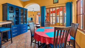 A dining area with a round table, chairs, a blue cabinet, and a window with curtains. - Golden Zone 5 Blocks to Beach - Groundfloor w Pool (Bucerías)