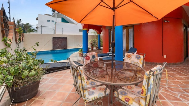 A patio with a round table and chairs, a potted plant, and an orange umbrella. - Golden Zone 5 Blocks to Beach - Groundfloor w Pool (Bucerías)