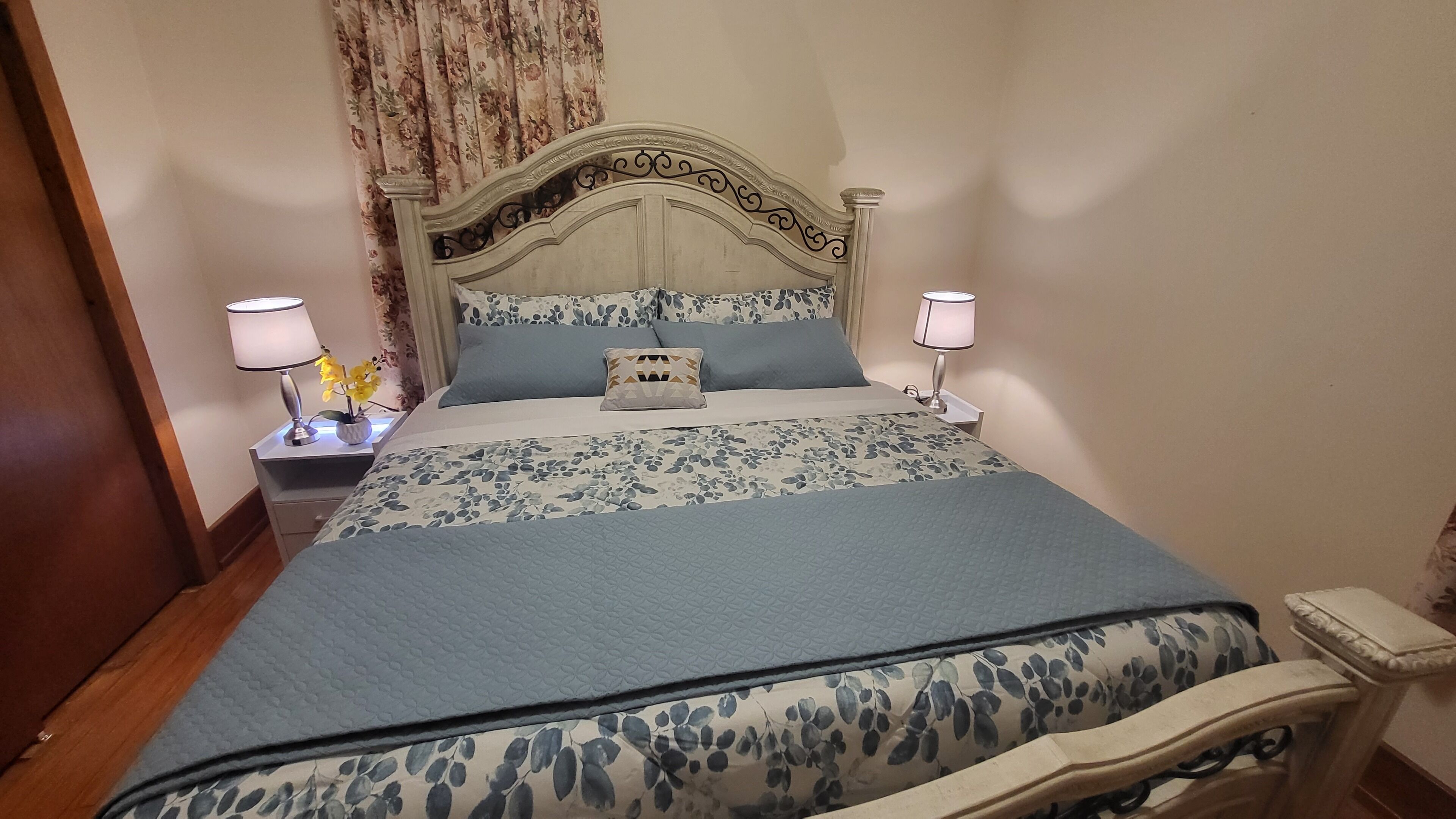 Una cama bien hecha con colcha estampada, dos lámparas de noche y una almohada decorativa.