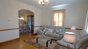 Una sala de estar con sofá, mesa de centro y lámpara. Se ve un comedor con mesa y sillas a través de un arco.