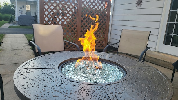 Una mesa metálica con hogar a leña, con un pozo de fuego de cristal en el centro, rodeada de sillas.