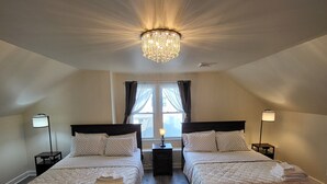 Un dormitorio con dos camas individuales, un candelabro, lámparas de noche y una ventana con cortinas.