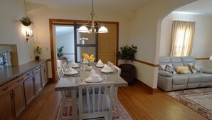 Un comedor con una mesa dispuesta para cuatro personas, un sofá y una cocina al fondo.