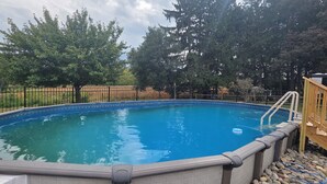 Una piscina rectangular con revestimiento azul, rodeada por una cerca de metal negro y árboles.