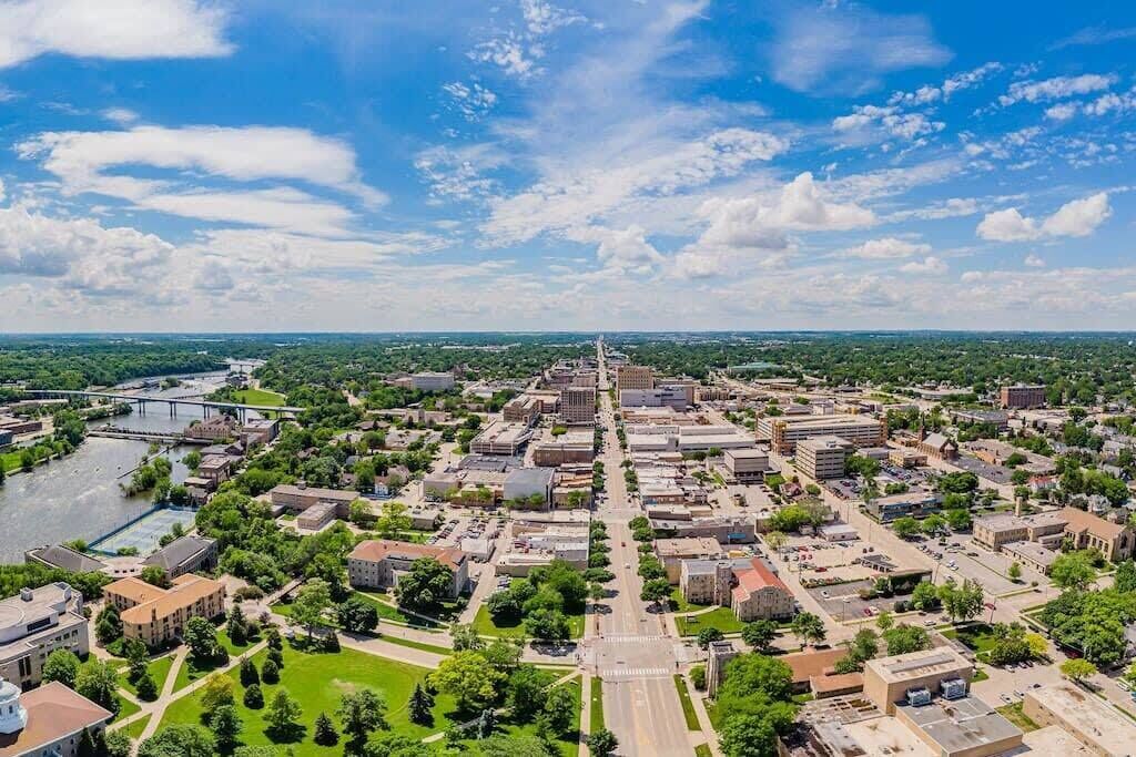 Vista aérea de una ciudad con un río, zonas verdes y una combinación de edificios comerciales y residenciales.
