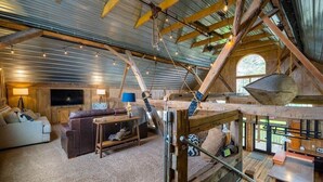 A rustic cabin interior with a lofted sleeping area, a cozy living room with a sofa and TV, and a dining area with a table and chairs. - Renovated Farmhouse w/ Game Barn & Firepit (Appleton)