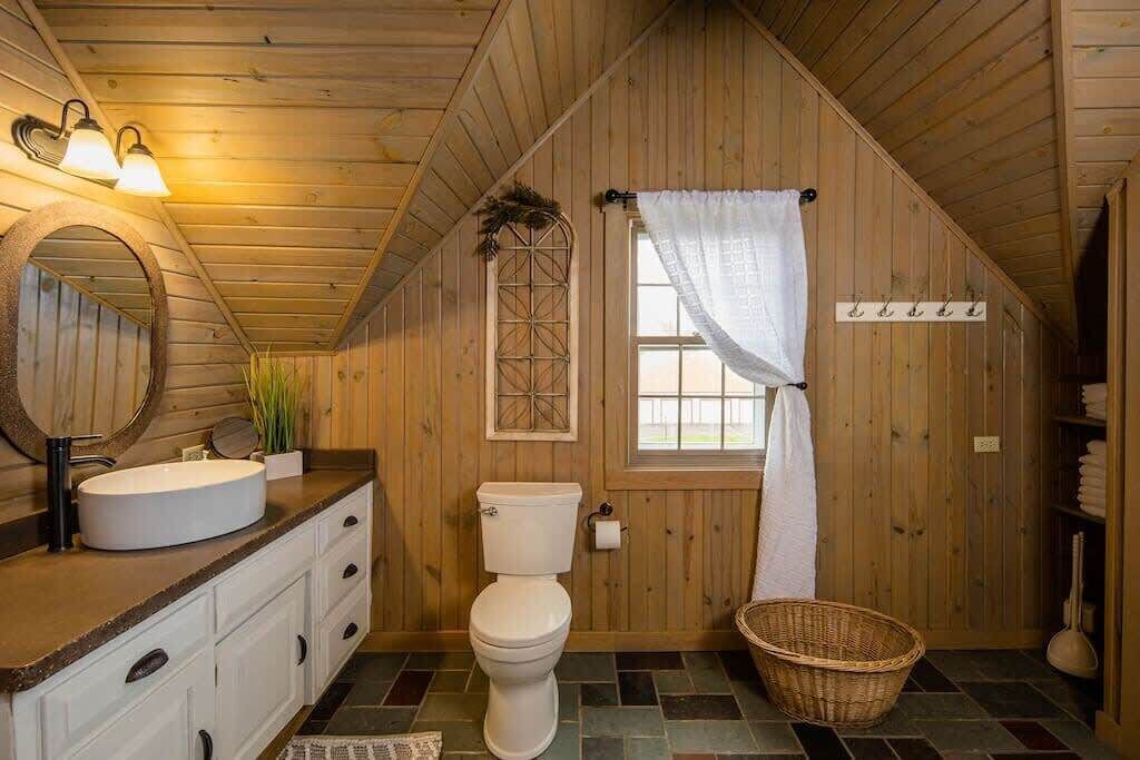 A wooden interior with a round mirror, white sink, and a white toilet.
