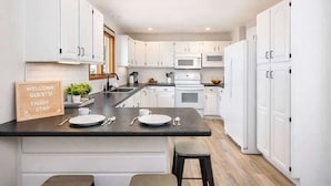 A modern kitchen with white cabinetry, a central island with a welcome sign, and a wooden floor. - Stylish Townhouse w/ Patio & Free Parking (Appleton)