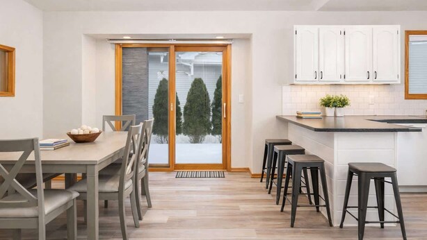 A modern kitchen with a dining area, featuring a large window with a view of trees and a snowy landscape. - Stylish Townhouse w/ Patio & Free Parking (Appleton)