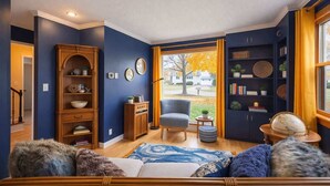 Ein Wohnzimmer mit einer Couch, einem Sessel, Holzregalen und Blick durch eine Tür.
