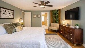 Ein Schlafzimmer mit Bett, Deckenventilator, Fernseher, Kommode und einer Tür zu einem anderen Raum.