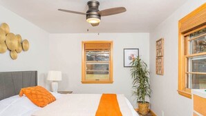 Camera da letto con un letto, una ventola a soffitto, una finestra, una pianta e una parete decorata.