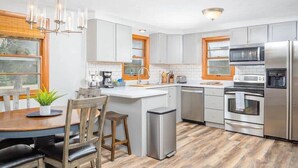 Una cucina moderna con mobili bianchi, elettrodomestici in acciaio inossidabile e un tavolo da pranzo in legno.