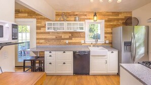 A modern kitchen with wooden accents, a dishwasher, a refrigerator, and a dining area with a table and chairs. - Remodeled Home Steps from Lawrence University (Appleton)