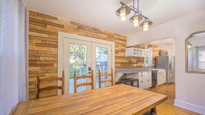 A dining area with a wooden table and chairs, a kitchen with white cabinets, and a hanging light fixture. - Remodeled Home Steps from Lawrence University (Appleton)