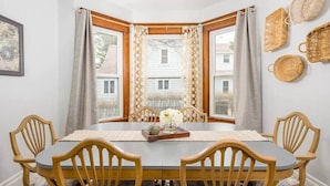A dining area with a wooden table and chairs, a vase with flowers, and a view through a bay window. - Family-Friendly Home Near Downtown & University (Appleton)