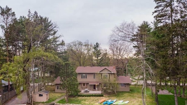 Una casa junto a un lago con kayaks, un muelle y un cobertizo pequeño.