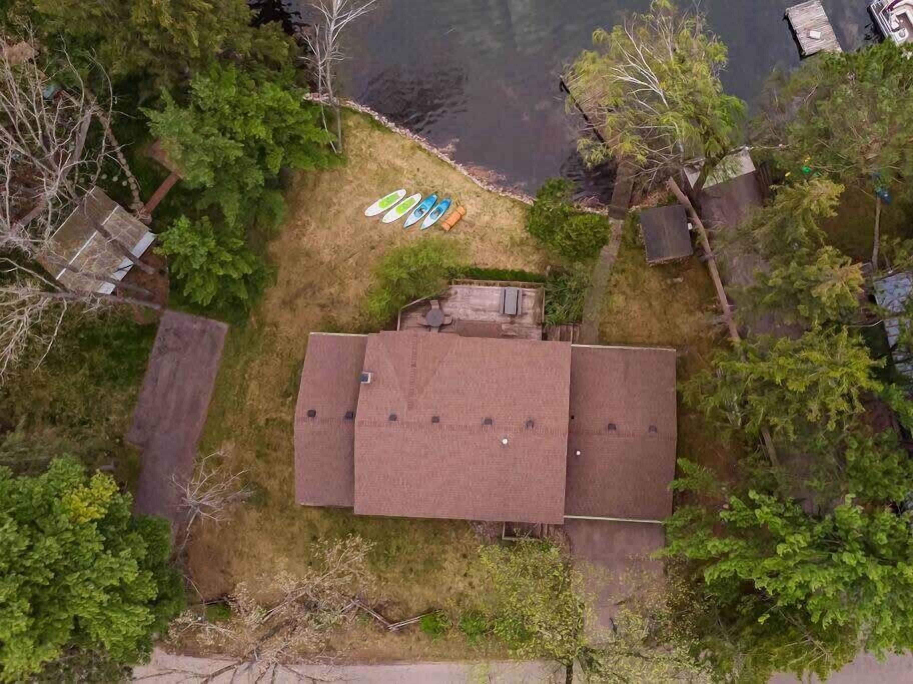 An aerial view of a property with a central building, a grassy area with surfboards, and surrounding trees.