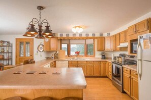 A kitchen with wooden cabinets, a central island, a stove, and a refrigerator. - Lakefront House w/ Kayaks & Private Dock (Waupaca)