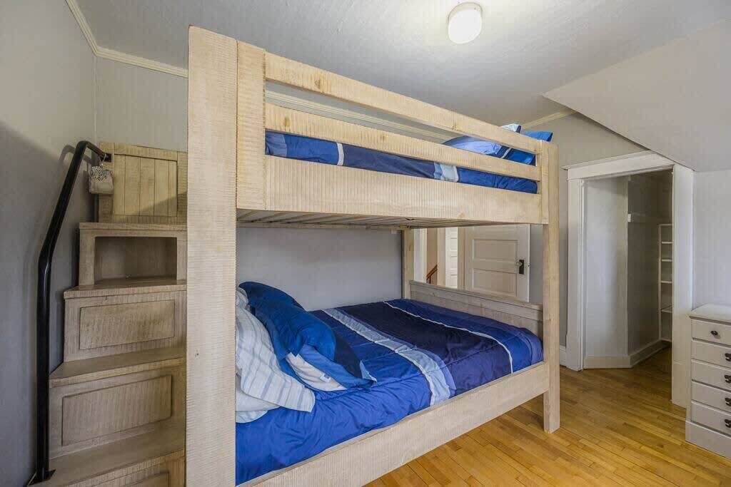 A bunk bed with a wooden frame and blue bedding. There is a wooden dresser to the left and a closet to the right.