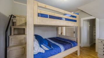 A bunk bed with a wooden frame and blue bedding. There is a wooden dresser to the left and a closet to the right.